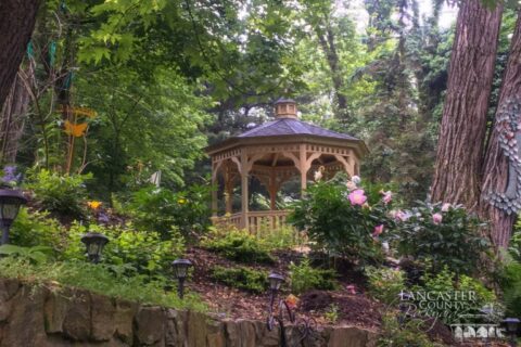 A Permanent Durable Gazebo In The Woods With Some Flowers Around It